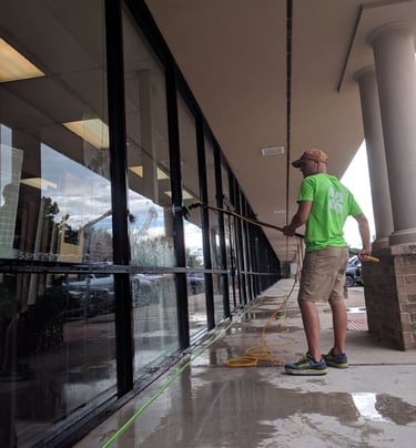 Technician in Clearly Organic Green uniform cleaning storefront windows with a water-fed pole