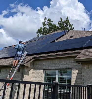 Technician cleaning solar panels on a residential roof with a squeegee pole
